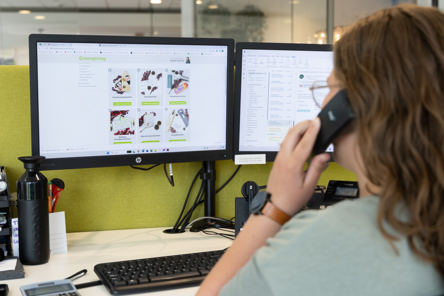 Greengiving-Mitarbeiter telefoniert am Schreibtisch mit dem Werbegeschenke-Webshop auf dem Bildschirm